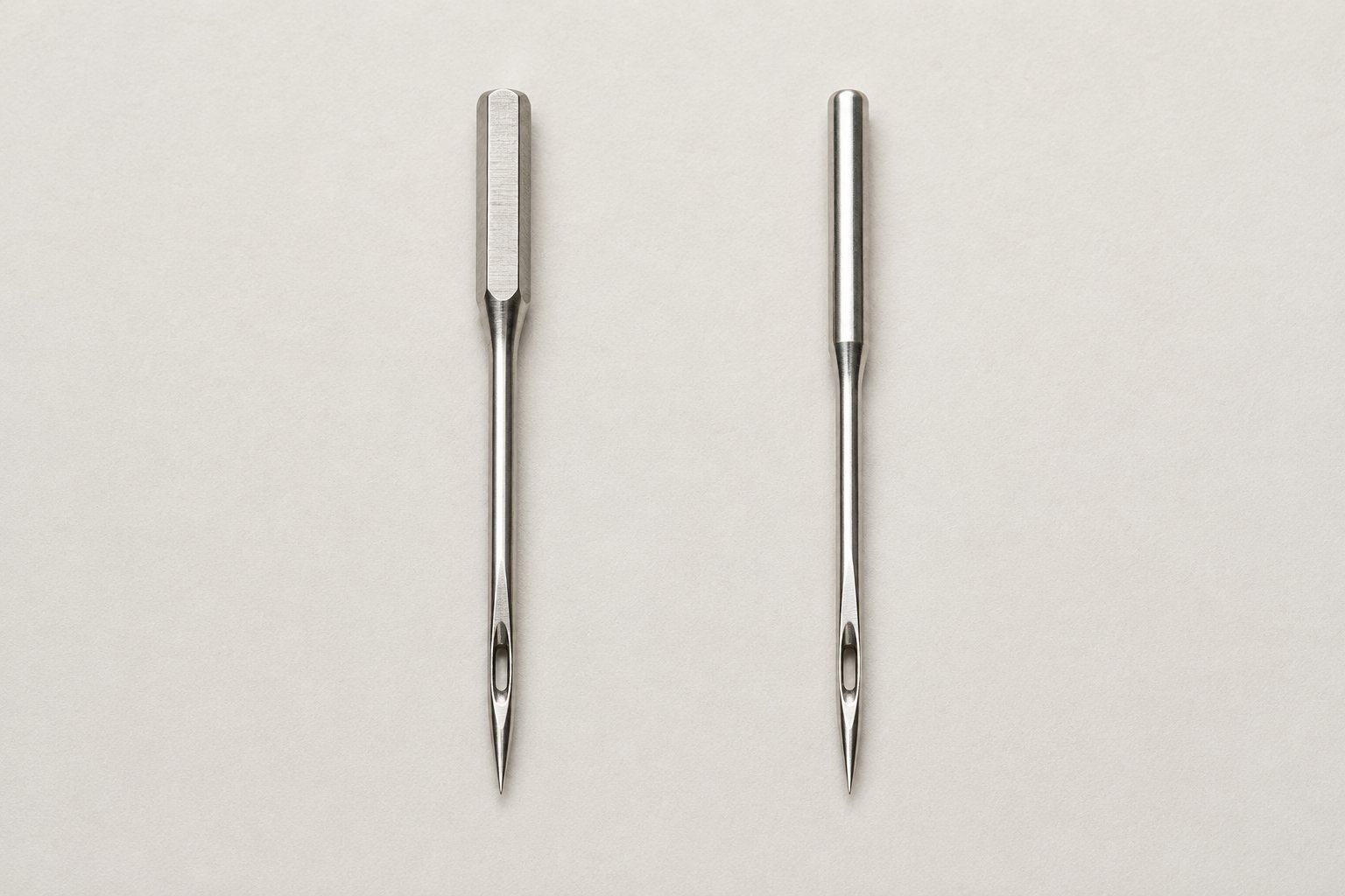 Flat-shank household sewing machine needle beside a round-shank industrial-style needle.